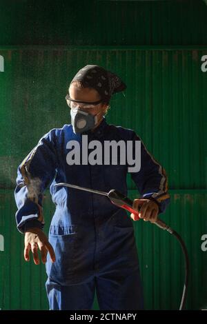 Konzentrierte weibliche Mechaniker in Uniform und Maske Kontrolle Luftkompressor Pistole vor der Arbeit Stockfoto