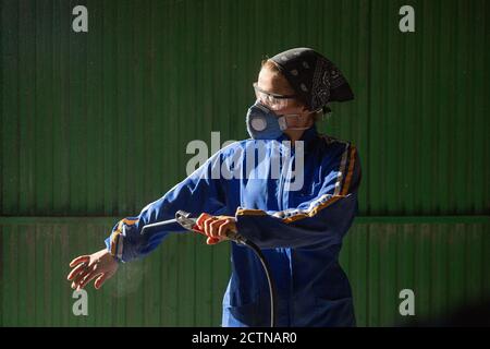 Konzentrierte weibliche Mechaniker in Uniform und Maske Kontrolle Luftkompressor Pistole vor der Arbeit Stockfoto