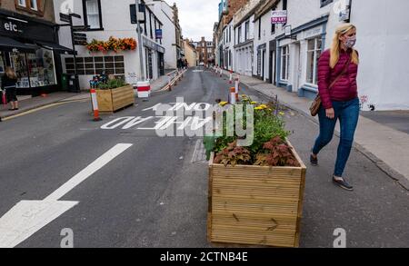 North Berwick, East Lothian, Schottland, Großbritannien, 24. September 2020. Die Covid-19 Coronavirus Pandemie Pflaster Verbreiterung Maßnahmen mit Straßenrand und Blumentöpfe in der engen High Street ermöglichen Fußgängern mehr Platz als eine Frau trägt eine Gesichtsmaske Spaziergänge entlang der Straße Stockfoto