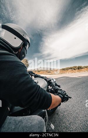 Rückansicht Cropped unkenntlich männlichen Fahrer in Lederjacke und Helm Reiten Motorrad am Straßenrand gegen bewölkten Himmel in der Landschaft Stockfoto