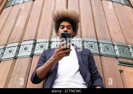 Von unten von einem afrikanischen Mann in Anzug mit seiner Handy vor einer Holzwand Stockfoto