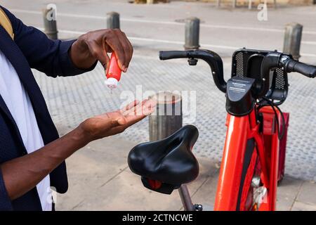 Detail eines schwarzen Mannes Hände mit Desinfektionsmittel Gel in Vor einem öffentlichen Fahrrad auf der Straße geparkt Stockfoto