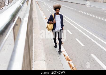 Afrikanischer Mann, der mit einer Tasche von seiner Schulter hängt Während Sie Musik mit einem schnurlosen Headset im hören Straße Stockfoto