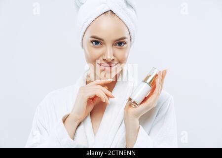 Junge Frau mit selbstbewussten Ausdruck, gesunde saubere glatte Haut, gepflegte Teint, hält Flasche Lotion oder Gel, berührt jawline, angezogen Stockfoto