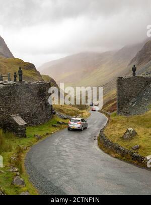 Honister Pass Summit - malerische Bergpassstraße im Lake District, England - Autos vorbei an Skulpturen auf beiden Seiten der Straße bei Honister Slate Mine Stockfoto