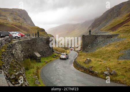 Honister Pass Summit - malerische Bergpassstraße im Lake District, England - Autos vorbei an Skulpturen auf beiden Seiten der Straße bei Honister Slate Mine Stockfoto