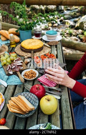 Hoher Winkel von nicht erkennbaren weiblichen Freundinnen, die am Holztisch sitzen Im Wald und Essen leckeres Essen während Picknick in Valle Del Jerte im Sommer Stockfoto