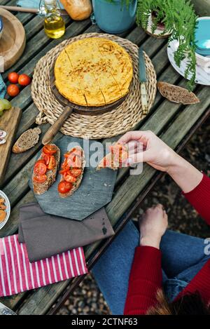 Hoher Winkel von nicht erkennbaren weiblichen Freundinnen, die am Holztisch sitzen Im Wald und Essen leckeres Essen während Picknick in Valle Del Jerte im Sommer Stockfoto