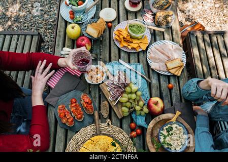 Hoher Winkel von nicht erkennbaren weiblichen Freundinnen, die am Holztisch sitzen Im Wald und Essen leckeres Essen während Picknick in Valle Del Jerte im Sommer Stockfoto