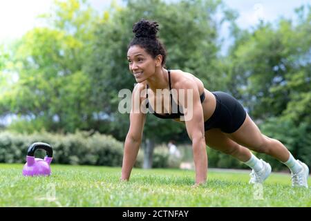 Starke afroamerikanische Athletin macht Liegestütze auf grün Rasen im Park, während Sie lächeln und wegschauen Stockfoto