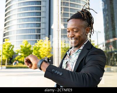 Low-Winkel-Seitenansicht des positiven afroamerikanischen männlichen Unternehmers Blick auf die Armbanduhr und Zeitkontrolle, während Sie in der Stadt stehen Und warten auf ein Meeting Stockfoto