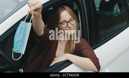 Junge kaukasische Frau, die medizinische Maske aus ihrem Auto wegwirft. Ende der covid-19 Pandemie. Hochwertige Fotos Stockfoto