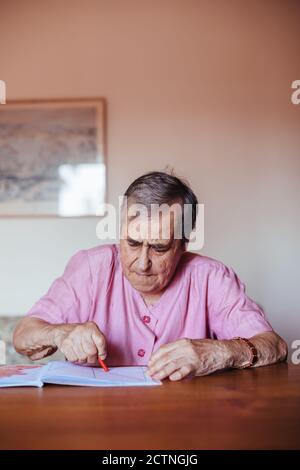 Vorderansicht einer älteren Frau mit Problemen bei der psychischen Alzheimer-Erkrankung, die auf einem Notizbuch in ihrem Haus gemalt wurde Stockfoto