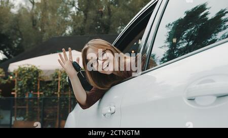 Happy Face Ausdruck der jungen kaukasischen Frau auf dem Fahrersitz sitzen und winken mit Autoschlüssel. Hochwertige Fotos Stockfoto