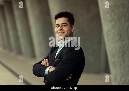 Inhalt schöner Geschäftsmann, der mit gekreuzten Armen in der Nähe des Gebäudes steht Stadt und Blick auf die Kamera Stockfoto
