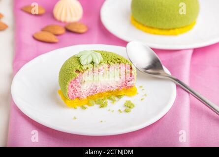 Grüner Mousse Kuchen mit Pistazien und Erdbeercreme auf weißem Holzhintergrund und rosa Textil. Seitenansicht, Nahaufnahme, selektiver Fokus. Stockfoto