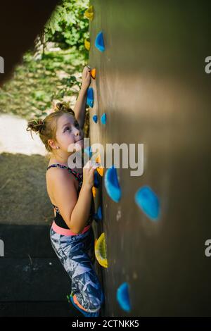 Seitenansicht des Kindes in Sportbekleidung Kletterwand mit künstlichen Rockt beim Training im Fitnessstudio und am Wochenende Stockfoto