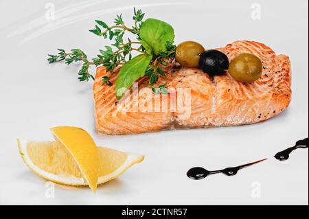 Portion frisch gekochtes leckeres Lachsfilet mit rotem Fischfilet mit Rosmarin, schwarzen und grünen Oliven, dekoriert mit Zitronenscheiben und Balsamico-Soße-Tropfen Stockfoto