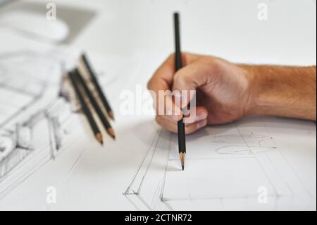 Grafiker und Künstler zeichnen mit der rechten Hand Architekturentwarf, mehrere schwarze Bleistifte im Hintergrund auf weißem Papier Stockfoto