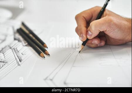 Grafiker und Künstler zeichnen mit der rechten Hand Architekturentwarf, mehrere schwarze Bleistifte im Hintergrund auf weißem Papier Stockfoto