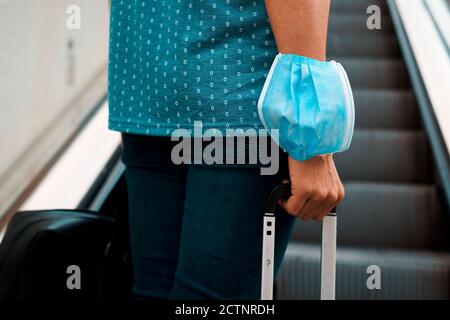 Nahaufnahme eines jungen Mannes auf einem Scalator, in Freizeitkleidung, mit einer Reisetasche in der einen Hand und einem Koffer in der anderen Hand, trägt ein Einweg-Gesicht ma Stockfoto