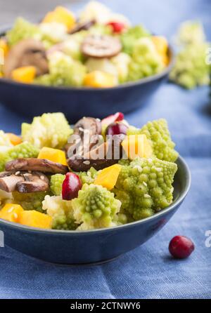 Vegetarischer Salat aus Romanesco-Kohl, Champignons, Preiselbeere, Avocado und Kürbis auf schwarzem Betongrund und blauem Textil. Seitenansicht, schließen Stockfoto