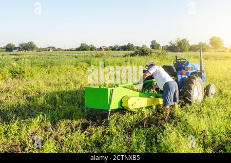 Ein Landwirt bedient einen Traktor auf einem Bauernhof Plantage Feld. Reparatur der Kartoffelgrabmaschine. Wartung von Anlagen und Maschinen. Unerwarteter Durchbruch Stockfoto