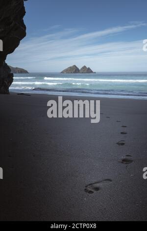 Fußabdrücke im Sand und der Blick auf Gull Rock Bilden Sie Holywell Cave am Holywell Bay Beach Stockfoto