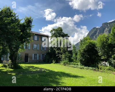 Ein altes französisches Herrenhaus mit Fensterläden und Rasen, im Hintergrund sind zerklüftete Hügel in der Region Ariège in Frankreich. Stockfoto