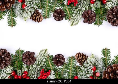 Weihnachtsrahmen mit schneebedeckten Tannenzweigen, Tannenzapfen und roten Holly Beeren auf weißem Hintergrund verziert. Traditionelle Neujahrsgeschichte. Winterurlaub Stockfoto