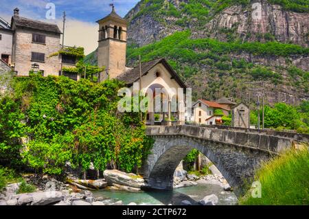 Brücke über einen Fluss mit rustikalem Haus und Kirche im Tal Maggia im Tessin, Schweiz. Stockfoto