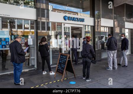 Fußgänger bilden eine Schlange vor einer Barclays Bank Filiale in der Edgware Road in London, während die Menschen den finanziellen Druck der Coronavirus-Pandemie spüren. Stockfoto