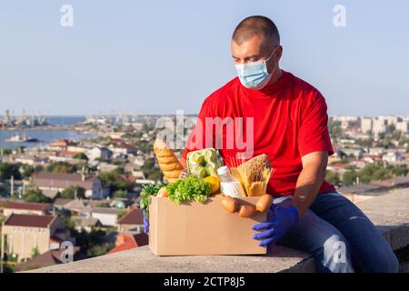 Delivery man in Schutzmaske und medizinische Handschuhe liefert frische Lebensmittel. Bereitstellungsdienst in Quarantäne Stockfoto