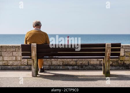 Mann saß auf einer Bank am Meer auf der Englische Küste Stockfoto