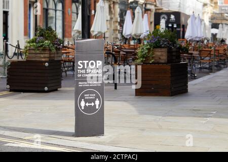 London, Großbritannien. - 21. September 2020: Ein Straßenschild - das Fußgänger zur sozialen Distanz auffordert - vor leeren Stühlen und Tischen im Freien eines Covent Garden Restaurants. Stockfoto