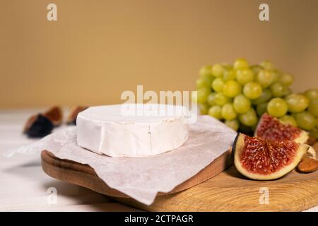 Camembert Käse auf Holzbrett, Zweig der grünen Trauben, Scheibe von Feigen und Nüssen. Stockfoto