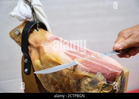 Älterer Mann schneidet iberischen Schinken mit einem Schinkenmesser. Spanisches Gastronomiekonzept. Stockfoto