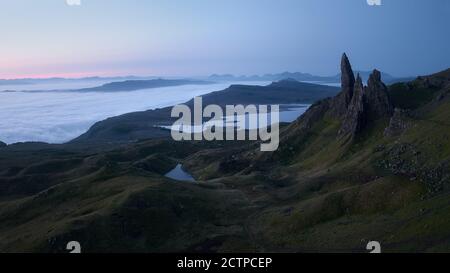 Atmosphärisch geheimnisvolle Top-Ansicht der hohen scharfen Klippen hoch über den Seen und das Meer mit niedrigen Wolken vor Sonnenaufgang bedeckt. The Old man of Storr, Isle of Skye, Schottland, Großbritannien. Stockfoto