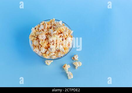 Eine transparente Schüssel Popcorn auf einer blauen Oberfläche. Heimfamilie beim Ansehen von Filmen. Speicherplatz kopieren. Stockfoto