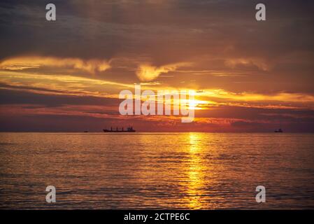 Sonnenuntergang am wolkenlosen Himmel auf dem Meer, Schiffe stehen am Horizont. Stockfoto