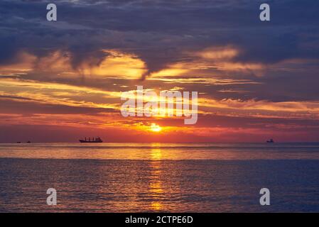 Sonnenuntergang am wolkenlosen Himmel auf dem Meer, Schiffe stehen am Horizont. Stockfoto