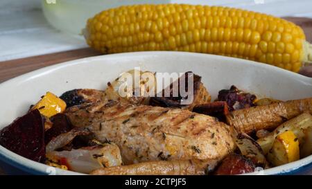 Ein gegrilltes Hähnchen sitzt auf einer Keramikplatte neben verschiedenen Wurzelgemüse. Verkohlte Linien aus dem Skillet-Muster sind deutlich sichtbar. Stockfoto