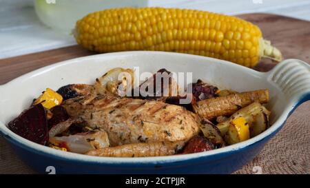 Ein gegrilltes Hähnchen sitzt auf einer Keramikplatte neben verschiedenen Wurzelgemüse. Verkohlte Linien aus dem Skillet-Muster sind deutlich sichtbar. Stockfoto