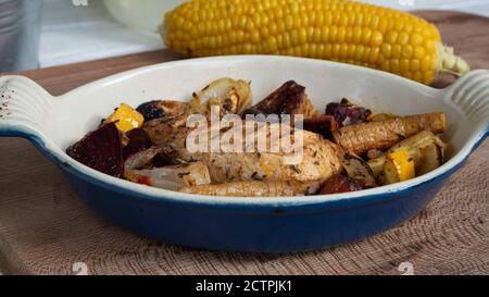 Ein gegrilltes Hähnchen sitzt auf einer Keramikplatte neben verschiedenen Wurzelgemüse. Verkohlte Linien aus dem Skillet-Muster sind deutlich sichtbar. Stockfoto