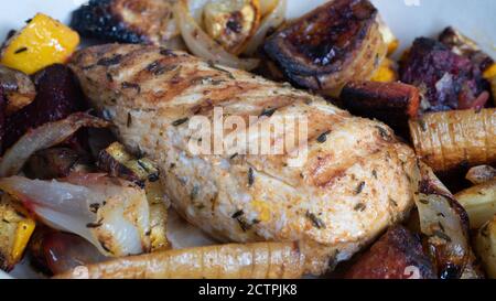 Ein gegrilltes Hähnchen sitzt auf einer Keramikplatte neben verschiedenen Wurzelgemüse. Verkohlte Linien aus dem Skillet-Muster sind deutlich sichtbar. Stockfoto