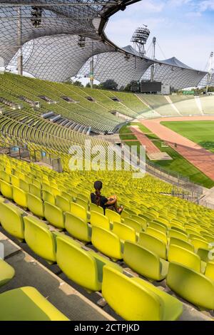München, Bayern / Deutschland - 17. September 2020: Eine alleinstehende Frau mit langen braunen Haaren sitzt allein in riesigen und leeren Stadion Stockfoto