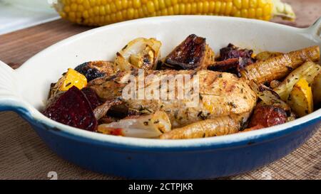 Ein gegrilltes Hähnchen sitzt auf einer Keramikplatte neben verschiedenen Wurzelgemüse. Verkohlte Linien aus dem Skillet-Muster sind deutlich sichtbar. Stockfoto