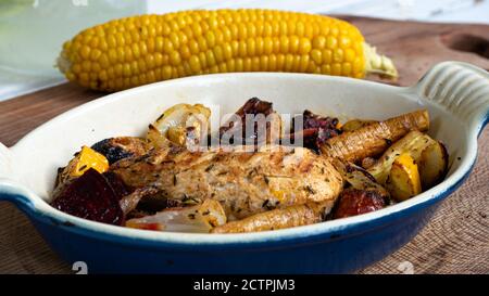 Ein gegrilltes Hähnchen sitzt auf einer Keramikplatte neben verschiedenen Wurzelgemüse. Verkohlte Linien aus dem Skillet-Muster sind deutlich sichtbar. Stockfoto