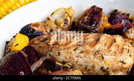 Ein gegrilltes Hähnchen sitzt auf einer Keramikplatte neben verschiedenen Wurzelgemüse. Verkohlte Linien aus dem Skillet-Muster sind deutlich sichtbar. Stockfoto