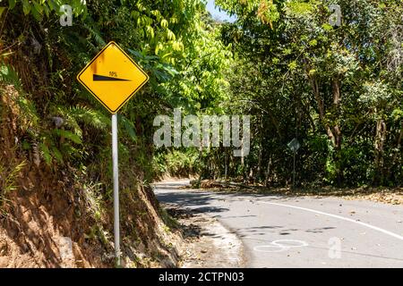 Gelbes, diamantförmiges Warnschild 'Steep Grade' an einer Abfahrtstraße im Tuaran District, Sabah, Malaysia. Stockfoto